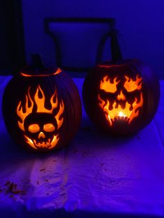 two carved pumpkins sitting on top of a table with blue light in the background