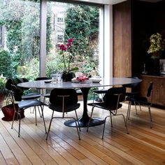 a dining room table with four chairs and a vase on the table in front of large windows