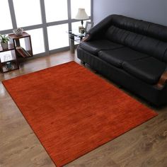 a living room with a black couch and red rug