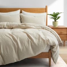 a bed with white sheets and pillows in a room next to a wooden nightstand holding a potted plant