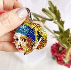 a person holding a beaded keychain with a flower in the back ground