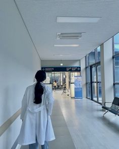 a woman walking down a hallway in an office building with lots of windows on both sides