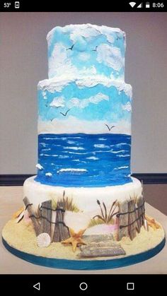 a three tiered cake with blue and white frosting on a table in front of a wall