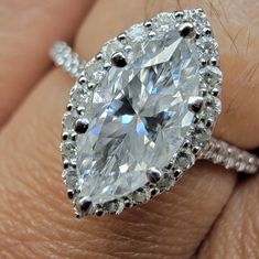 a woman's hand holding an engagement ring with a pear shaped diamond in the center