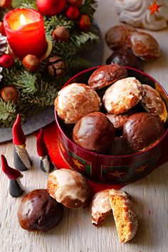 a red tin filled with chocolate covered donuts next to some christmas decorations and candles