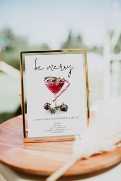 a card on a wooden table with a white feather sitting next to it and the words be merry written in cursive writing