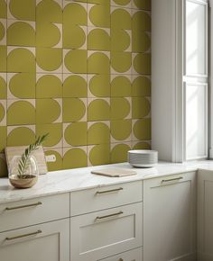 a kitchen with yellow and white tiles on the wall next to a potted plant