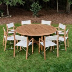 a round wooden table with white chairs around it in the middle of some green grass