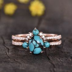 a turquoise and white stone ring sitting on top of a piece of wood with flowers in the background