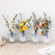 three vases filled with flowers sitting on top of a lace covered tablecloth next to a book