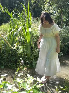 a girl with dark hair and light skin wearing a long white dress with short puff sleeves is standing in a small clear stream of water surrounded by tall green plants with a forest in the distance Whimsical Garden Outfit, French Countryside Aesthetic Outfits, Aesthetic Cottage Core Outfits, French Countryside Outfit, Cottegcore Outfit, Gardencore Outfit, Naturecore Aesthetic Outfit, Farmcore Outfit