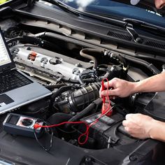 a man is working on his laptop in front of the engine bay with an open hood