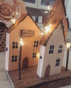 two wooden houses with fairy lights on them and a rose in the background, sitting on a table