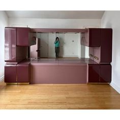 a woman standing in front of a mirror on top of a wooden floor next to purple cabinets