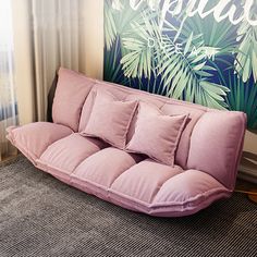 a pink futon couch sitting in front of a tropical wall hanging on the wall