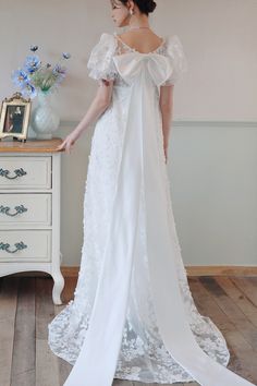 a woman in a white wedding dress standing next to a dresser with flowers on it