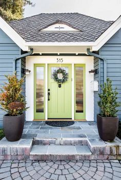 a green front door with two planters on the steps