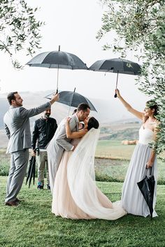 a bride and groom kissing under umbrellas in front of their wedding party on the grass