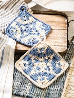 two crocheted squares sitting on top of a wooden table next to a plate