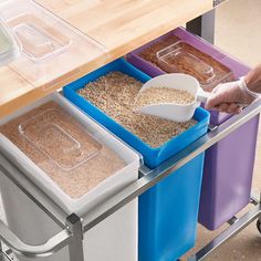 a person scooping cereal into three bins on a metal cart with blue and purple containers