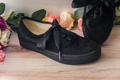 a pair of black shoes sitting on top of a wooden floor next to pink flowers