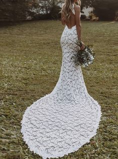 a woman in a white wedding dress standing on grass with her back to the camera