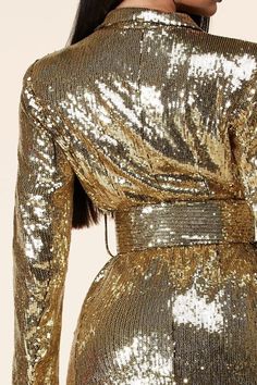 a woman wearing a gold sequin dress with long sleeves and an open neckline