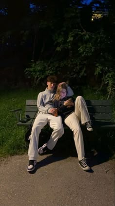 two people are sitting on a bench in the park, one is hugging the other