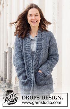 a woman standing in front of a white building wearing a blue sweater and cardigan