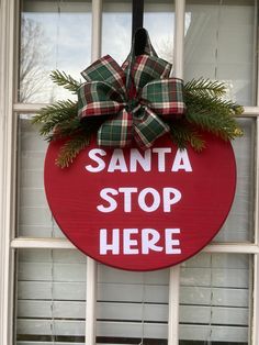 a red santa stop sign hanging on the side of a window with a green bow