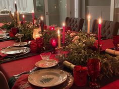 a dining room table set for christmas dinner with candles and greenery on the table