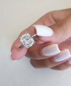 a woman's hand holding an engagement ring with a square diamond in the center