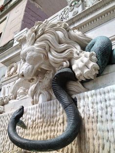 a statue of a lion on the side of a building with a snake crawling out of it's mouth