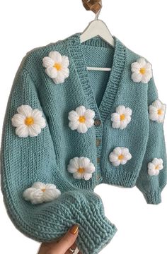 a person holding up a blue sweater with white flowers on the front and back of it