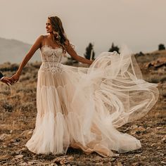 a bride and groom holding hands while walking through an open field with mountains in the background