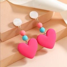 two heart shaped earrings on top of a pink box next to a white bow tie