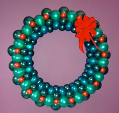 a wreath made out of green, orange and blue balloons with a red bow on top