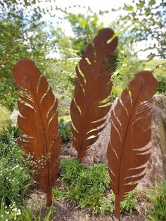 three metal feathers sitting on top of a lush green field