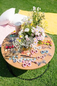 a wooden table topped with lots of flowers on top of a lush green field next to a yellow blanket