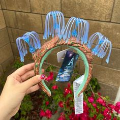 a hand holding up a blue and green hair comb with flowers in the background,