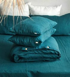 a stack of pillows sitting on top of a bed next to a plant in a vase