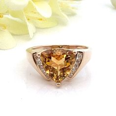 This beautiful honey yellow citrine and diamond ring is solid 14k yellow gold. There are 10 diamonds - 5 on each side of the citrine. They are channel set.  Ring Size: 7.5 - can be sized Metal Content: 14k yellow gold Gemstone: Trillion Cut Citrine Carat: 3 ct Size in mm: 10 x 10 x 6.38 Diamonds: 10 Round Brilliant Cut diamonds Carat: .10 ctw Clarity: SI2 Color: H/I Measurements: Face of Ring (North South): 11mm  Height of ring off of finger: 8mm Band / Shank Width: 2mm Weight: 4.9 Grams Stamps: P14k  Condition: Excellent Estate Items will ship in gift box or pouch Each piece is thoroughly examined and refinished as needed by our professional jewelers, tested to guarantee metal content,  graded by our in-house GIA (Gemological Institute of America) Graduate Gemologist, and inspected for qu Orange Diamond Accented Jewelry For Weddings, Orange Diamond Jewelry With Diamond Accents, Yellow Gold Citrine Diamond Ring With Accents, Yellow Gold Diamond Ring With Citrine Accents, Trillion Cut Topaz Jewelry For Anniversary, Yellow 14k Gold Jewelry With Diamond Accents, Fine Jewelry Citrine Diamond Ring With Accent Stones, Fine Jewelry Yellow Gold Topaz Ring With Diamond Accents, Classic Citrine Jewelry With Diamond Accents