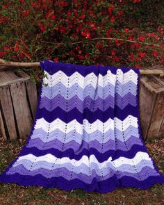 a purple and white crocheted blanket sitting on top of a wooden fence next to red flowers