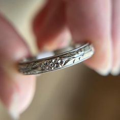 a close up of a person's hand holding a silver ring with flowers on it