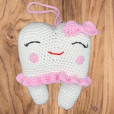 a crocheted tooth shaped ornament hanging on a wooden surface with a pink ribbon