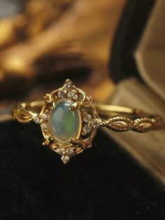 an opal and diamond ring sits on top of a black velvet box with gold trimming