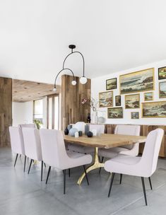 a dining room table with white chairs and pictures on the wall behind it in an open space