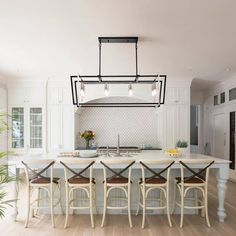 a large kitchen island with chairs around it and lights hanging from the ceiling over it