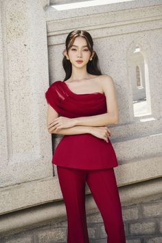 a woman standing in front of a stone wall wearing a red top and matching pants