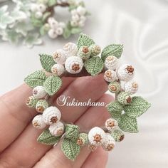 crocheted white flowers and green leaves are arranged in the shape of a heart